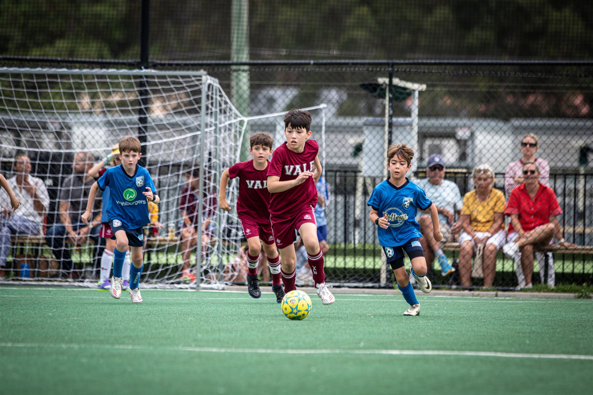 Vale player driving through midfield with defenders in pursuit, goal net behind